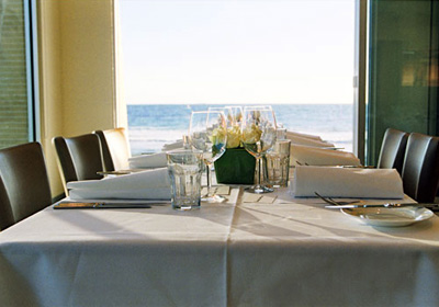 White table cloth, nicely set table, and a view of the ocean.